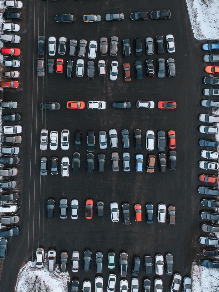 Drone shot capturing a top-down view of a busy parking lot with multiple vehicles in winter.